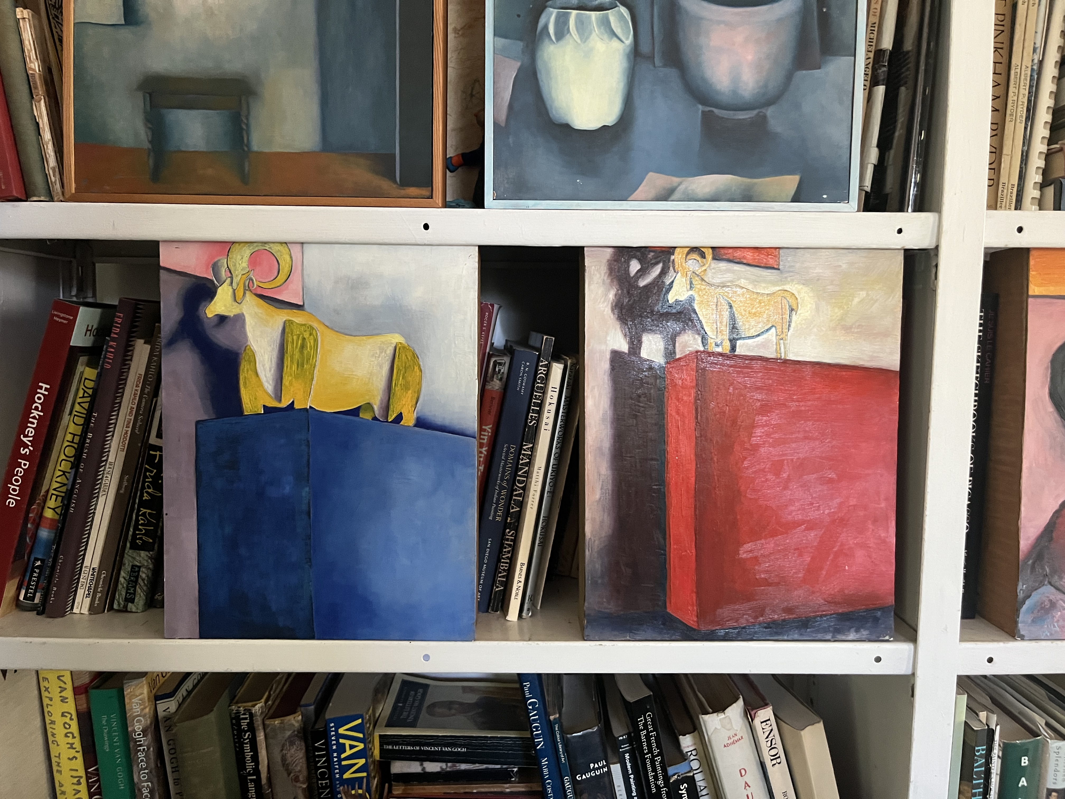 Ram paintings on bookshelves — yellow ram on blue, ram on red — flanked by art books